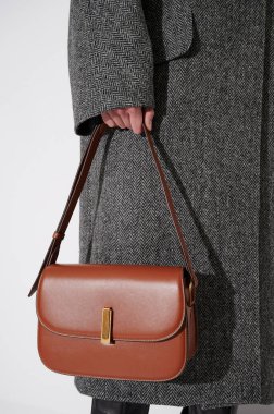 Gri ceketli, kahverengi çantalı bir kız. Lüks klasik el çantası kızların elinde. Modaya uygun aksesuarlar. Dikey fotoğraf. Yakın çekim..