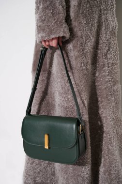 Yeşil deri çantalı, gri kürklü bir kız. Lüks klasik el çantası kızların elinde. Modaya uygun aksesuarlar. Dikey fotoğraf. Yakın çekim..