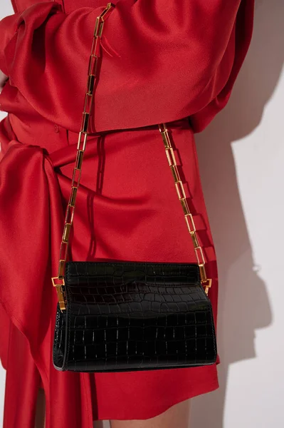 ゴールドチェーンと美しいブラックレザーハンドバッグと赤いドレスの女の子 洗練された高級ハンドバッグで爬虫類効果 ファッショナブルなアクセサリー 垂直写真 — ストック写真