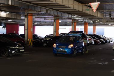Park yerinde kaza geçirmiş. Küçük mavi araba hasar gördü. Acil durum arabası sinyali açık. Yol işareti ver..