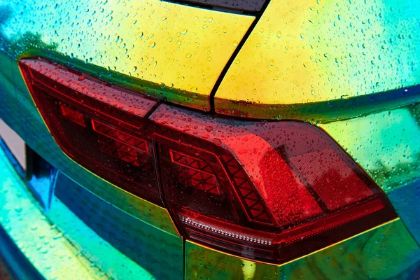 Chameleon holographic colour car in the rain. Rear view closeup. Beautiful modern LED backlights closeup. Car wrapping with iridescent paint. Raindrops on the car.