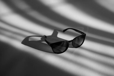 Beyaz arka planda gölgeli siyah güneş gözlüğü. Güneşli bir günde gradyanı olan plastik bardaklar. Siyah beyaz fotoğraf.
