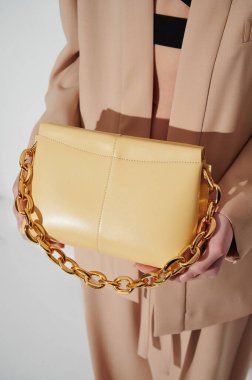 Güzel bej takım elbiseli, elinde büyük altın zincirli, lüks sarı deri çantalı bir kız. Dikey moda fotoğrafı. - Yakın çekim. Alışveriş konsepti fotoğrafı. Logo veya reklam için boş alan.