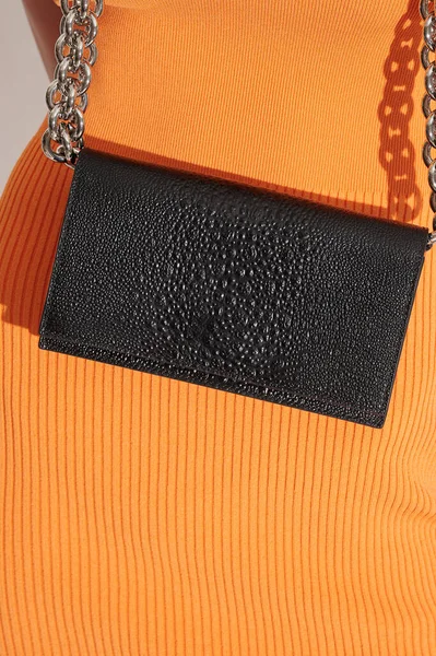 Woman in orange dress with black leather handbag. Luxury bag made from embossed leather with reptile effect with huge metal chain. Closeup front view. Free space for logo or text.