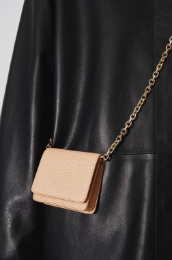 Altın bir zincir üzerinde bej deri kabartmalı çapraz vücut cüzdanı. Siyah deri ceketli adam. Küçük deri bir çanta. Sığır derisi. Dikey fotoğraf yakın plan.