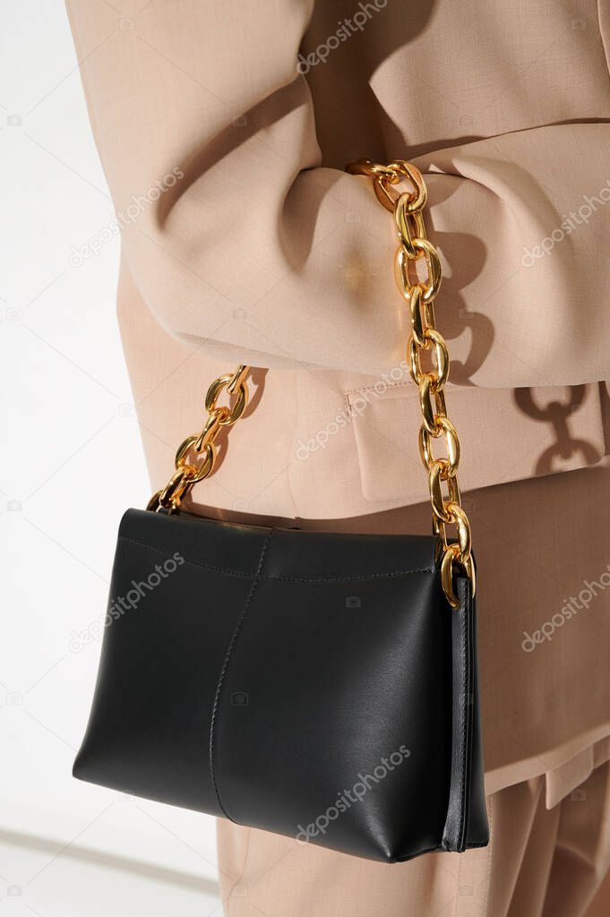 Woman in a beige suit with black leather handbag with massive golden chain. Vertical photo closeup. Hard light. Crossbody bag.