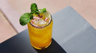 Pembe yuvarlak şeker ve nane ile süslenmiş ferahlatıcı güzel bir limonata. Balkonda buzlu sarı kokteyl. Yaz içeceği. Geniş web biçimi fotoğrafı.