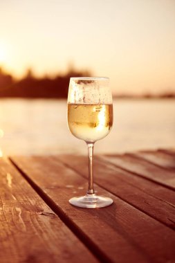 Gün batımında şampanya bardağında beyaz şarap. Ahşap iskelede köpüklü soğuk şampanya. Ilık ışıkla tek bir içki. Rahatla konsept fotoğraf. Dikey fotoğraf.