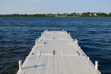 Mavi gölün üzerindeki beyaz ahşap iskele. Denizde güneşli bir gün ve boş bir rıhtım. Sahil görünümü.