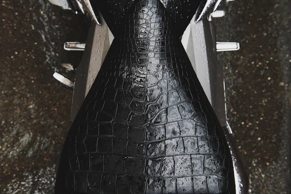 Motorcycle black leather seat after the rain. Natural reptile leather covered with raindrops. Stylish bike closeup. View from above.