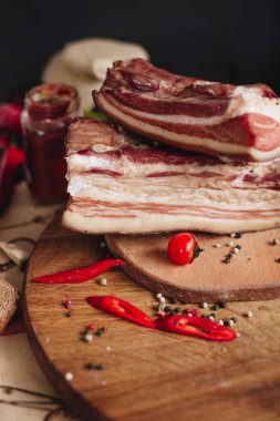 Koca bir parça pastırma, bir kavanoz yaban turpu, kırmızı biber parçaları ve mutfak masasındaki ahşap bir tahtada sarımsak..