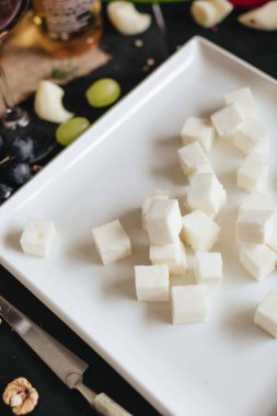 Siyah mutfak masasında beyaz tabakta beyaz peynir küpleri yığını..