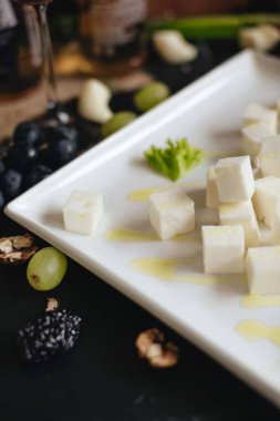 Beyaz tabakta beyaz peynir küpleri ve siyah mutfak masasında bir bardak şarap..