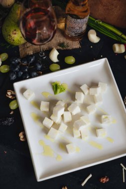 Beyaz tabakta beyaz peynir küpleri ve siyah mutfak masasında bir bardak şarap..