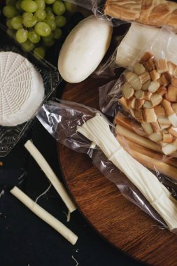 Siyah arka planda tahta bir tahtanın üzerinde peynir çeşitleri. Mozzarella, füme peynir.. 