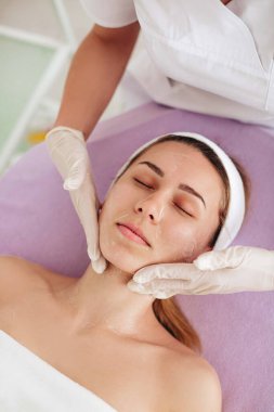 Güzellik uzmanı, kozmetoloji kliniğindeki yüz bakımını yeniledikten sonra kadının yüzüne krem sürüyor. Genç kadın yaşlanma ve cilt bakımı için kaldırılıyor.. 