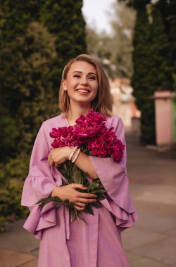 Bir buket şakayıkla şık, mor bir elbiseyle gülümseyen mutlu bir kız. Moda, yaşam tarzı konsepti. 