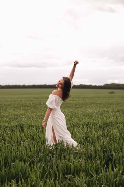 Beyaz keten elbiseli güzel bir esmer kız buğday tarlasında dans ediyor. Tarlada şık bir kız..