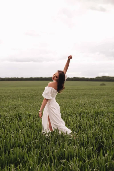 Beyaz keten elbiseli güzel bir esmer kız buğday tarlasında dans ediyor. Tarlada şık bir kız..