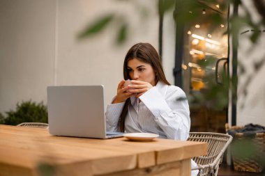 Çay içen ve uzaktan kumandalı bir bilgisayarla yeşil bir kazağa sarılmış bir kadın. Modern iş hayatında düşünce, karar verme ve yaratıcılık kavramı.