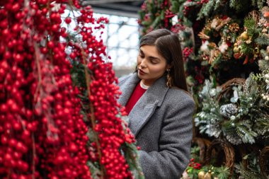 Açık hava tatil pazarında kırmızı böğürtlen ve Noel süslerini inceleyen genç bir kadın..