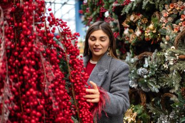 Açık hava tatil pazarında kırmızı böğürtlen ve Noel süslerini inceleyen genç bir kadın..