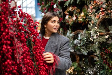Açık hava tatil pazarında kırmızı böğürtlen ve Noel süslerini inceleyen genç bir kadın..