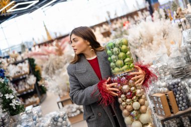 Noel süslemeleriyle dolu bir tatil mağazasında alışveriş yaparken büyük konteynırlar taşıyan genç bir kadın..