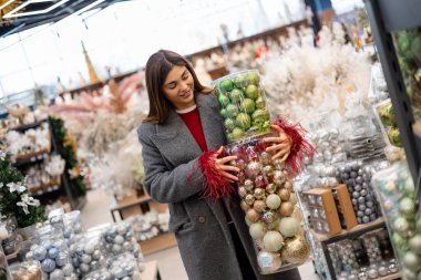 Noel süslemeleriyle dolu bir tatil mağazasında alışveriş yaparken büyük konteynırlar taşıyan genç bir kadın..