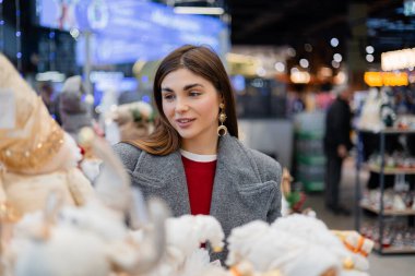 Noel oyuncakları ve şenlikli dekorasyonları seçen genç bir kadın mevsimlik süslerle çevrili bir tatil mağazasında..