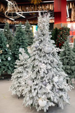 Dondurulmuş yapay Noel ağacı bir mağazada beyaz ve gümüş süslerle süslenmiş..