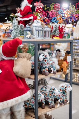 Noel fenerleri ve mevsimlik süsler arasında raflarda sergilenen yumuşak oyuncak atlar ve tatil süslemeleri.