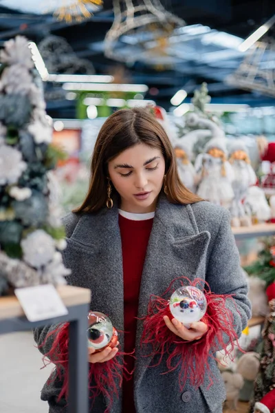 Noel süsleriyle dolu bir bayram mağazasında alışveriş yaparken iki Noel kar küresi karşılaştıran genç bir kadın..