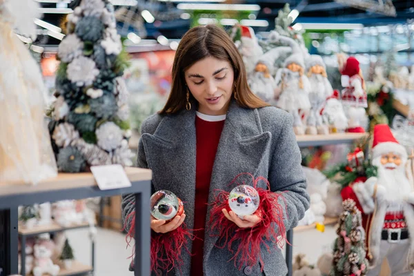 Noel süsleriyle dolu bir bayram mağazasında alışveriş yaparken iki Noel kar küresi karşılaştıran genç bir kadın..