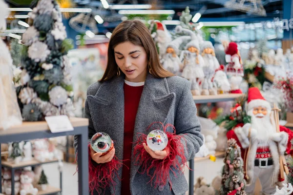 Noel süsleriyle dolu bir bayram mağazasında alışveriş yaparken iki Noel kar küresi karşılaştıran genç bir kadın..