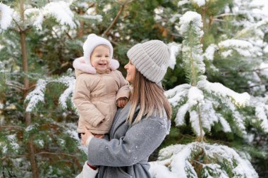 Anne gülen bebeğini karlı bir çam ormanında tutuyor. Sıcak kış anı neşe ve bağlarla dolu.