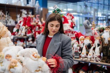 Raflardaki dekoratif yumuşak figürlere bakan genç bir kadın. Çeşitli konforlu eşyalar ve parlak arka plan ışıklarıyla kapalı perakende sahne.
