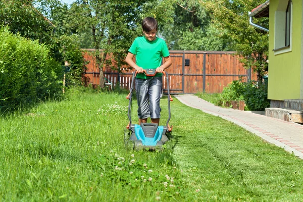Chico cortando hierba alrededor de la casa en verano — Foto de Stock