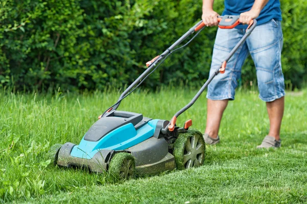 Muž sečení trávníku s modrými sekačka v létě — Stock fotografie