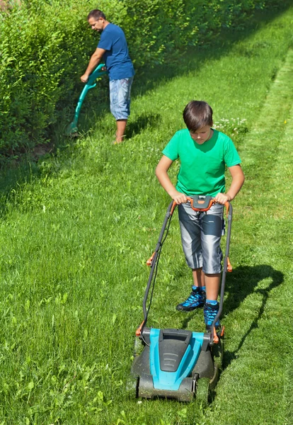 Мальчик стрижет газон с мужчиной, стригущим по краям — стоковое фото