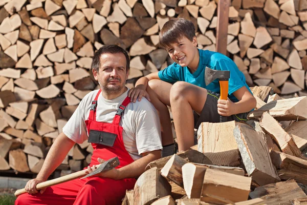 Father and son resting on pile of chopped wood — Stock Photo, Image