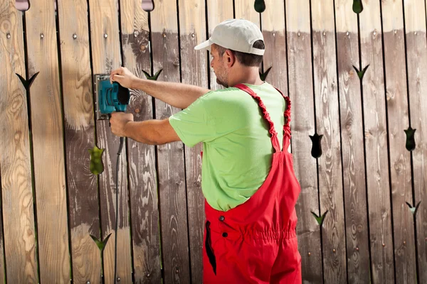 Worker scraping old cracked paint from wooden fence with power t — Stock Photo, Image