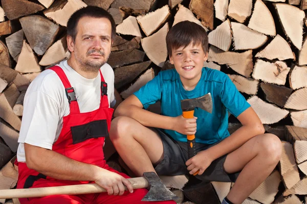 Man and boy sitting together in front of chopped wood — Stock Photo, Image
