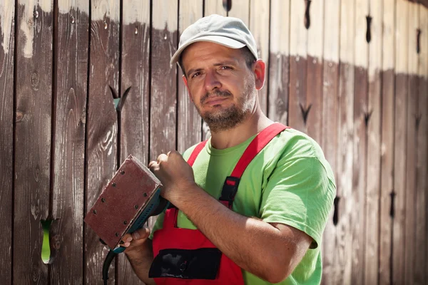 Arbeiter dabei, die alte Farbe von einem Holzzaun abzukratzen — Stockfoto