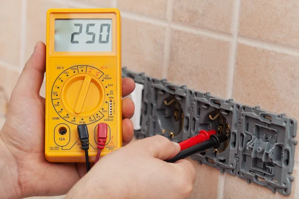 Electrician hands with multimeter measuring the voltage in a wal — Stock Photo, Image