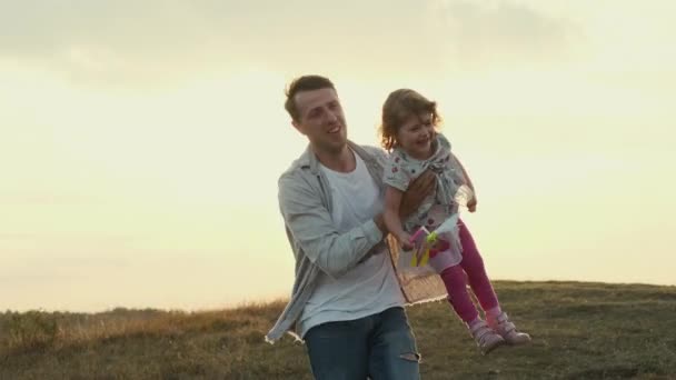 Vacaciones en familia en la naturaleza. Papá tuerce a su hija en sus brazos como si estuviera volando. — Vídeo de stock