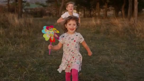 Linda niñita corriendo en el campo. Ella tiene en sus manos molino de viento de juguete girando desde el viento. — Vídeo de stock