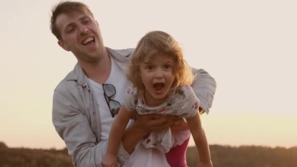 Vacaciones en familia en la naturaleza. Papá tuerce a su hija en sus brazos como si estuviera volando. — Vídeo de stock