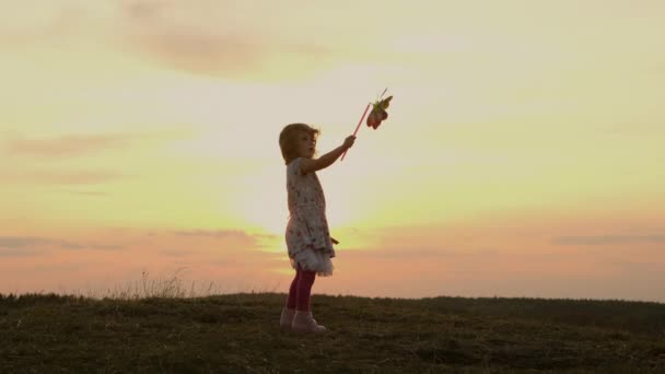 Κοριτσάκι που στέκεται στη φύση στο ηλιοβασίλεμα. Ανεμόμυλος — Αρχείο Βίντεο