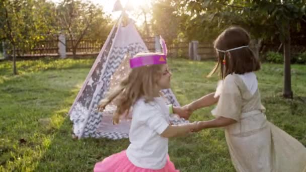 Feriado das crianças. Duas meninas bonitas em trajes de índios dançando segurando as mãos no jardim. — Vídeo de Stock